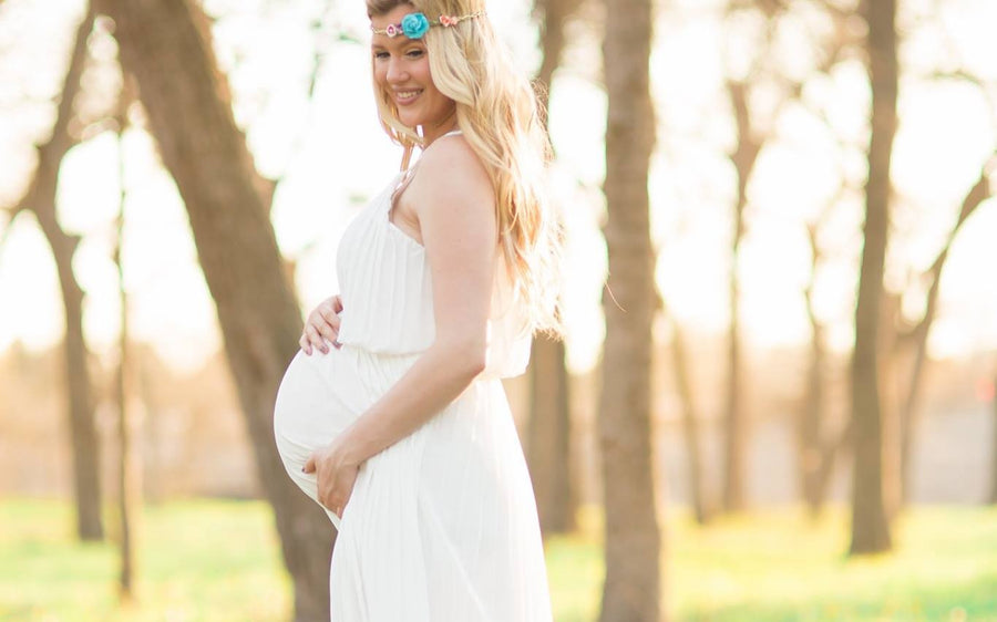 Holly Tanella, pregnant, in a white dress among trees in golden evening light